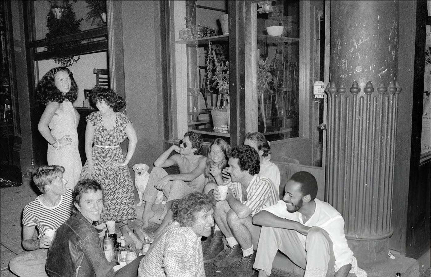 A group of people sits on the sidewalk and have a party outside the Food restaurant in SoHo during the blackout, 1977.
