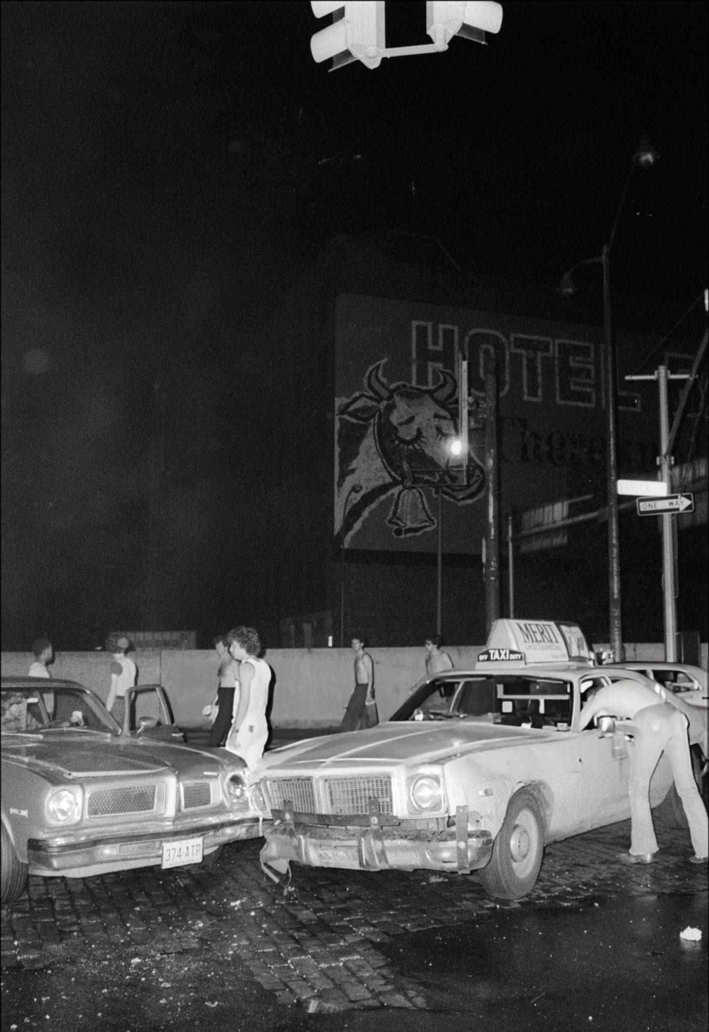 Pedestrians and onlookers stand around the site of a traffic accident during a blackout, 1977.