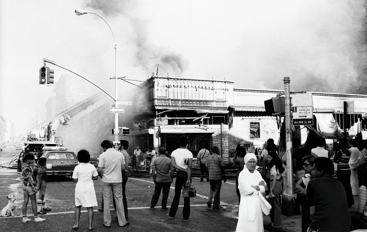 People look on as firemen put out arsonist's handiwork on Marmion Ave. in Brooklyn during the blackout, 1977.