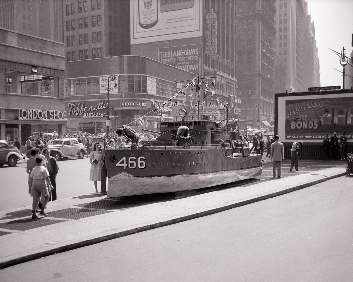 U.S. Navy destroyer mockup acts as a recruiting station beside a "Buy War Bonds" billboard poster, Times Square, NYC, 1940s.