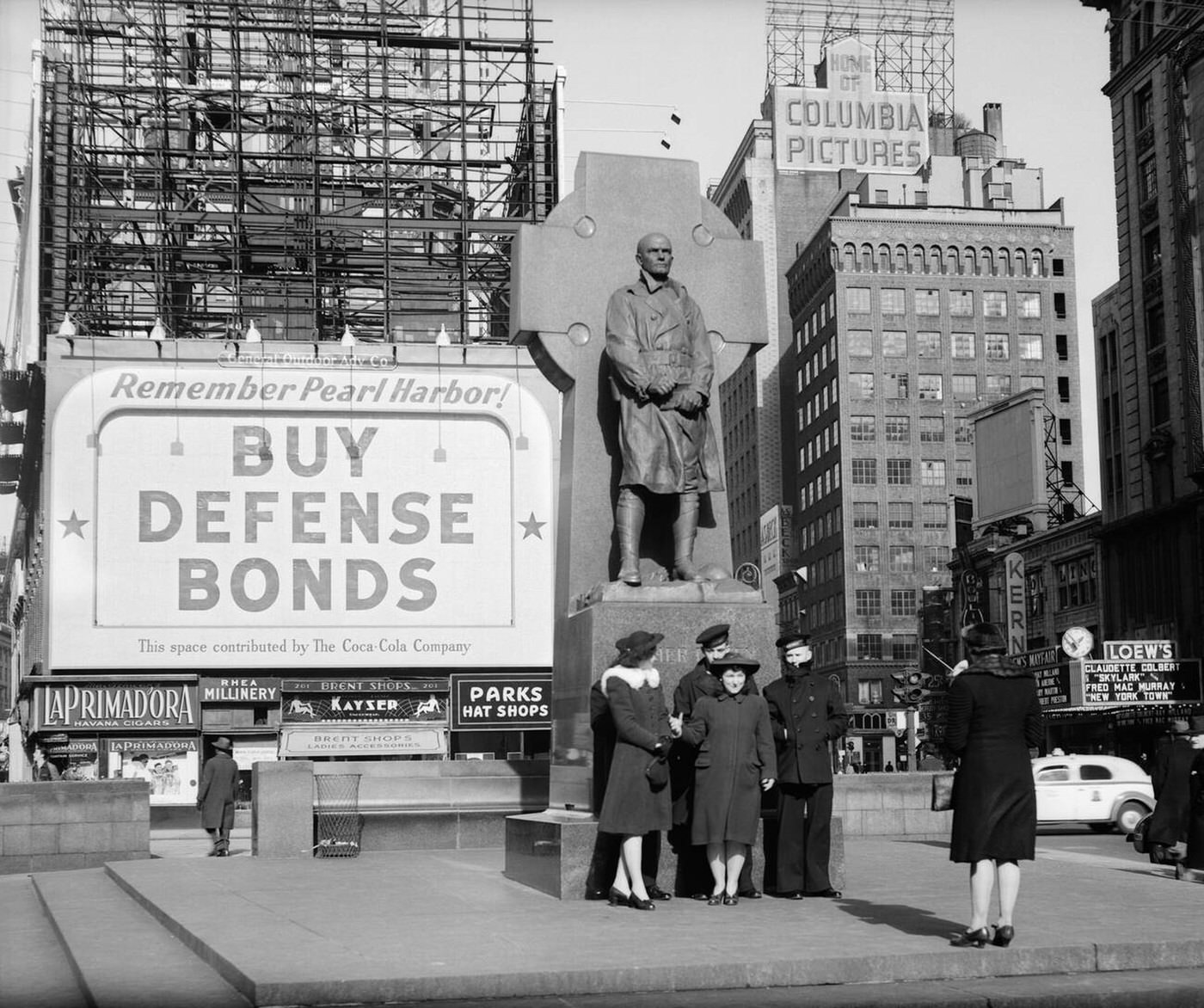 Sailors and women pose at Father Duffy Statue "Buy Defense Bonds" billboard, Times Square, New York City, 1942.