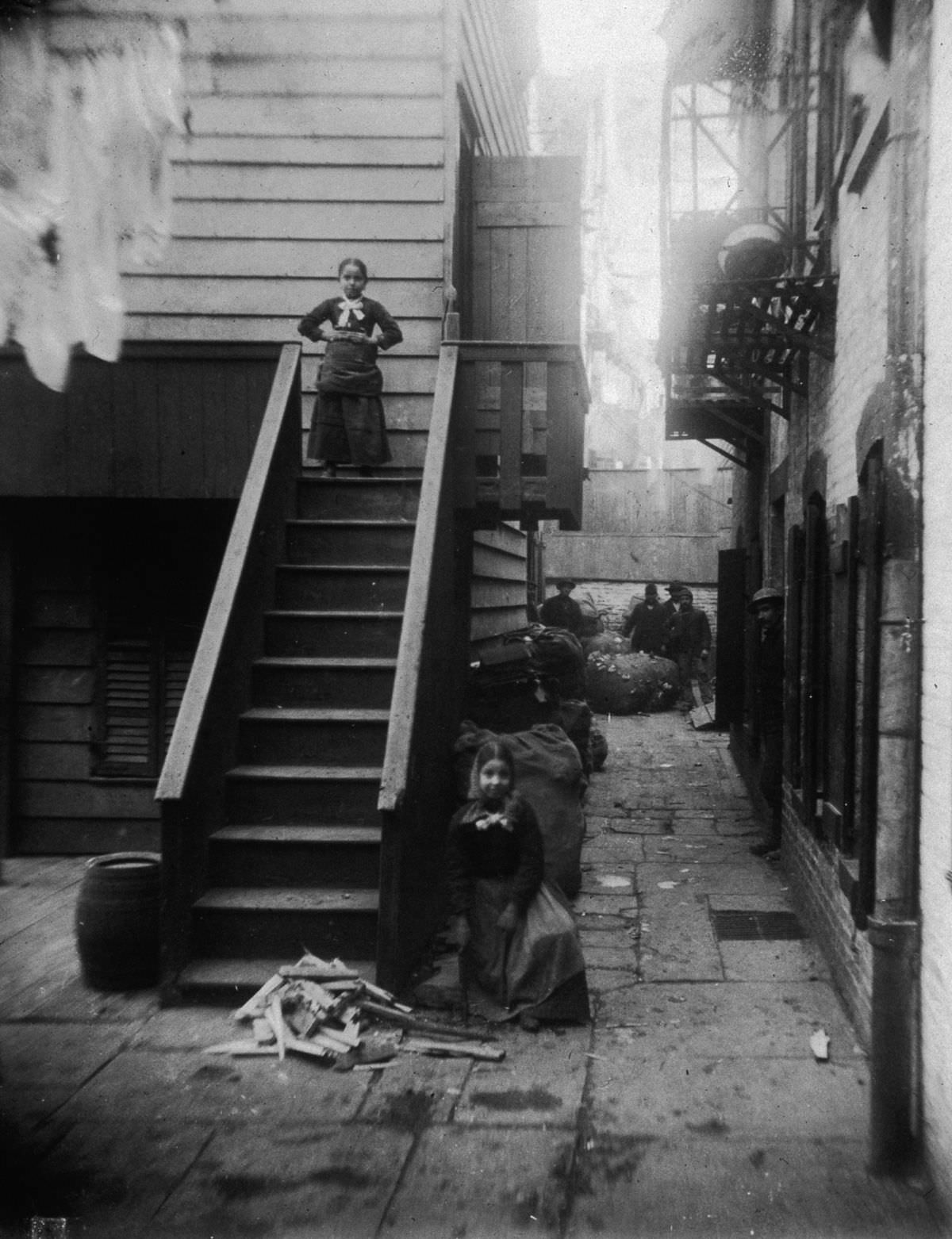 Two young ragpickers stand at a staircase in Baxter Alley, in Little Italy, 1890.