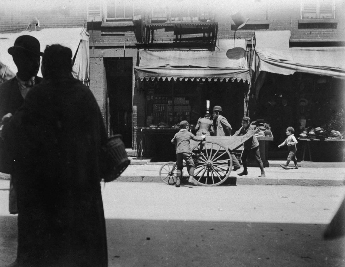 Two young boys steal items from a vendor's pushcart on Hester Street in the Lower East Side, 1895.