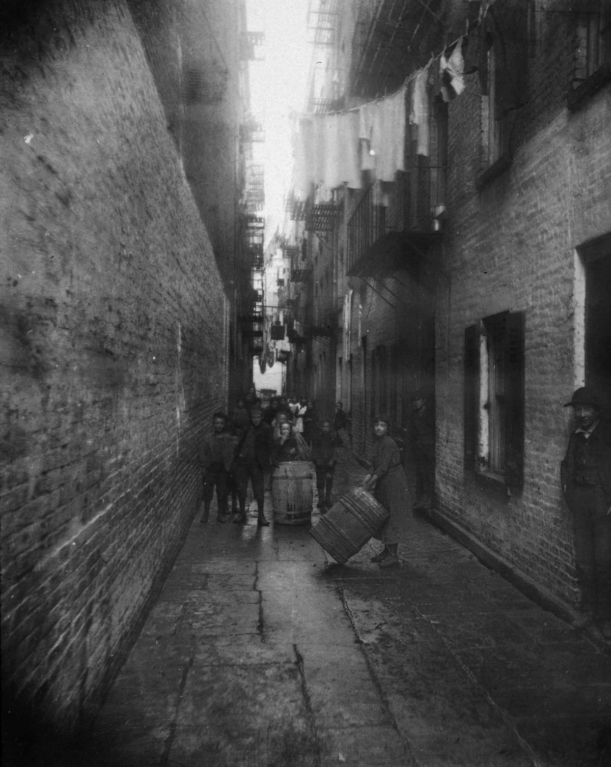 Children play with barrels in an alley between tenement buildings in Gotham Court, 38 Cherry Street, 1890.