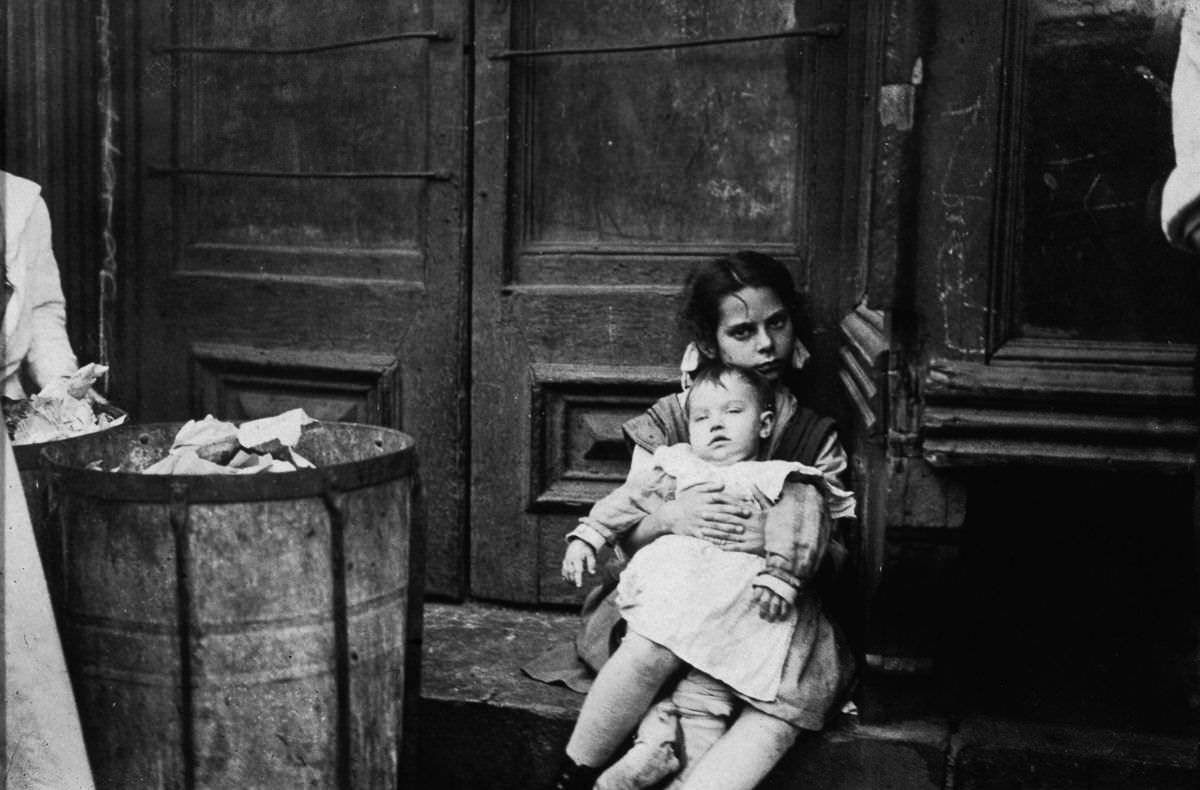 A young girl holds a baby in a doorway, 1890.