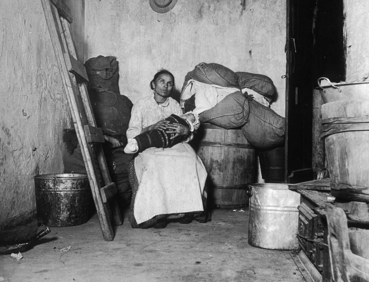 An Italian immigrant rag-picker sits with her baby in a small run-down tenement room on Jersey Street, 1887.