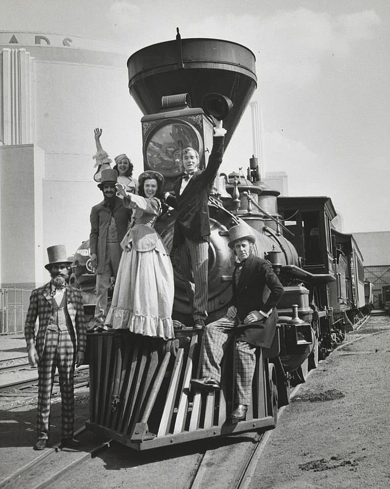 Actors in various costumes on the front of a steam engine.