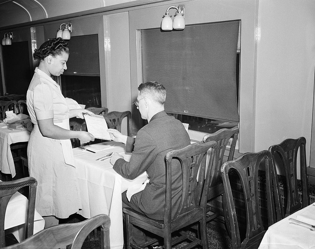 Waitress presenting a menu to a passenger in the dining car at Penn Station, 1943.
