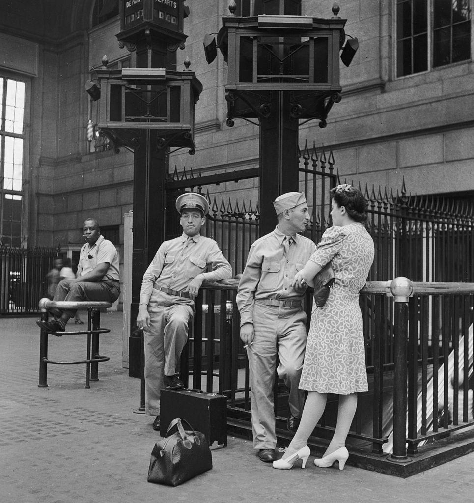 Soldiers smoke and stand with a young woman while waiting in the Pennsylvania railroad station, New York City, 1942.