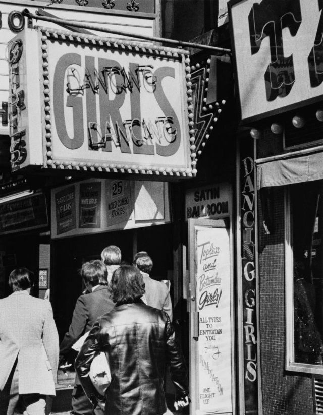 Men pass by a strip club entrance in Times Square, 1975.
