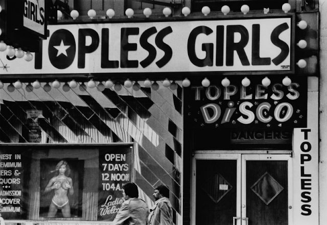 Two men walk past a topless disco in New York City, circa 1980.