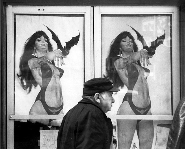 An elderly man walks past explicit signs featuring a cartoon of a scantily clad woman, New York, 1981.