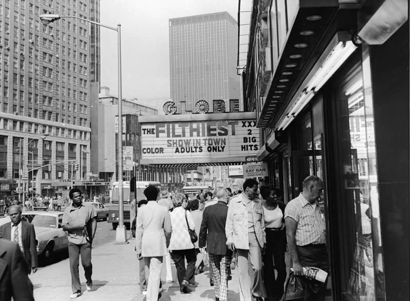 Tourists peer into shop windows as they walk past a theater advertising “The Filthiest Show in Town,” Times Square, 1975.