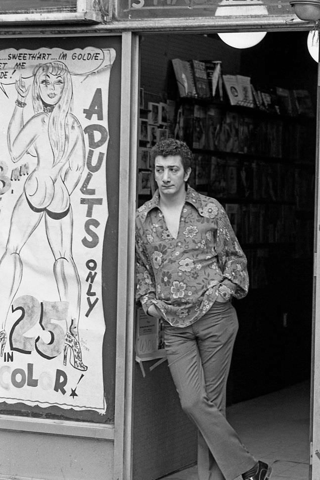 A sex shop clerk watches foot traffic pass by, waiting for the next customer, 1970.