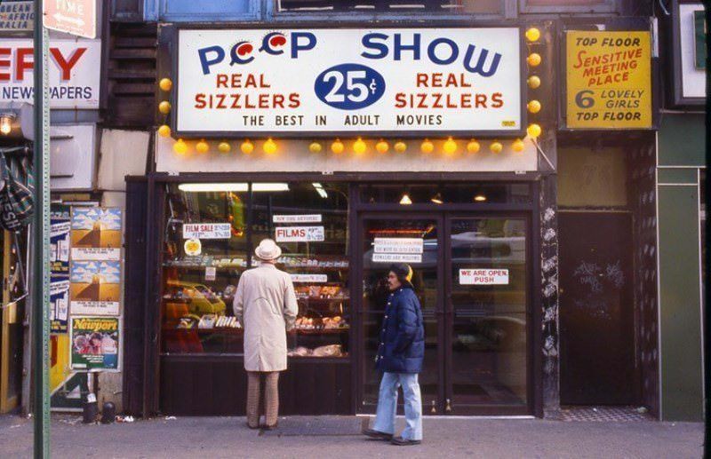 A man browses a peep show window beside a sign advertising a “sensitive meeting place” with “lovely girls.” Brothels, often run by organized crime, operated openly without legal consequence.