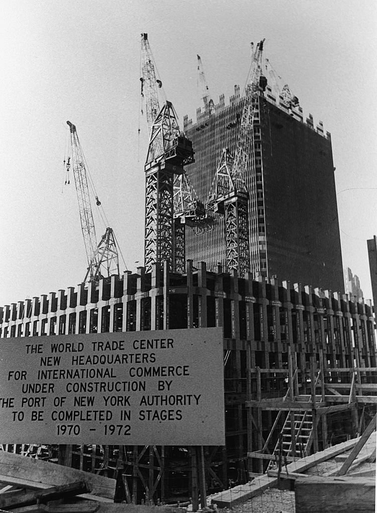 View of the World Trade Center under construction, with a sign announcing the completion schedule, 1969.