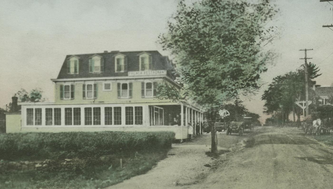 Burbank Hotel, with a sign on the roof for a "French Restaurant," an old car in the street, and people posed by and on the front porch, near the railroad station in Great Kills, Staten Island.