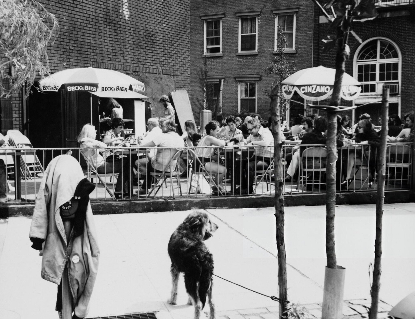 Al Fresco Dining Outside A Cafe With Diners Beneath Parasols Marked 'Beck'S Bier' And 'Cinzano' On Sixth Avenue In Greenwich Village, Manhattan, 1974.