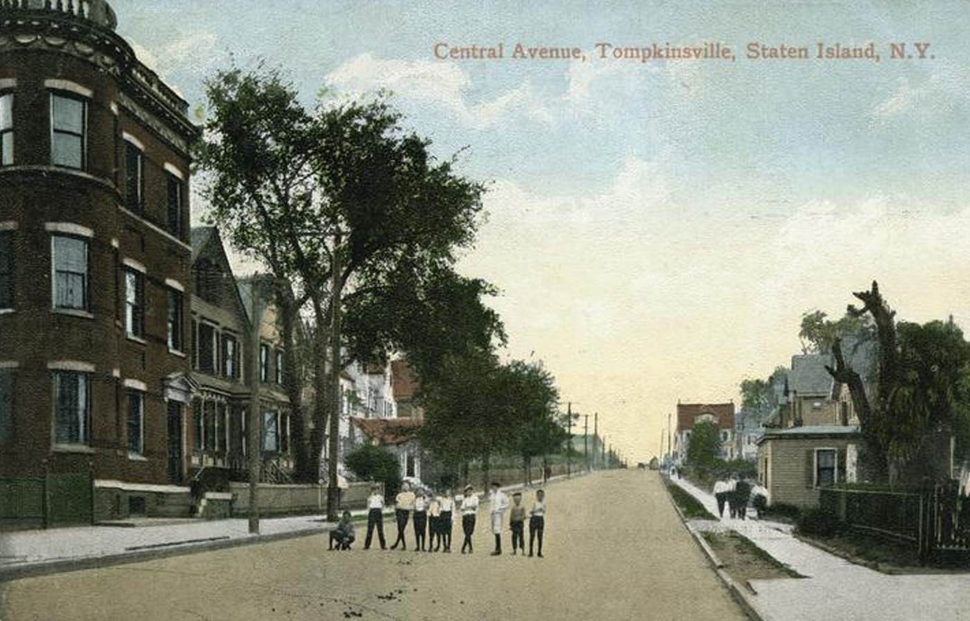 Central Avenue, Tompkinsville, showing a residential street with row homes, a three-story brick apartment building, people walking on the street, and ten children posed in a line in the street.