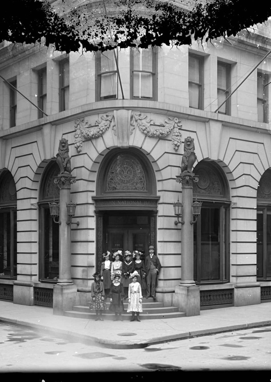 A Man And Seven Young Girls Pose In Front Of The Entrance To The Western National Bank Of The City Of New York, 13 Nassau Street, Ca. 1900S.