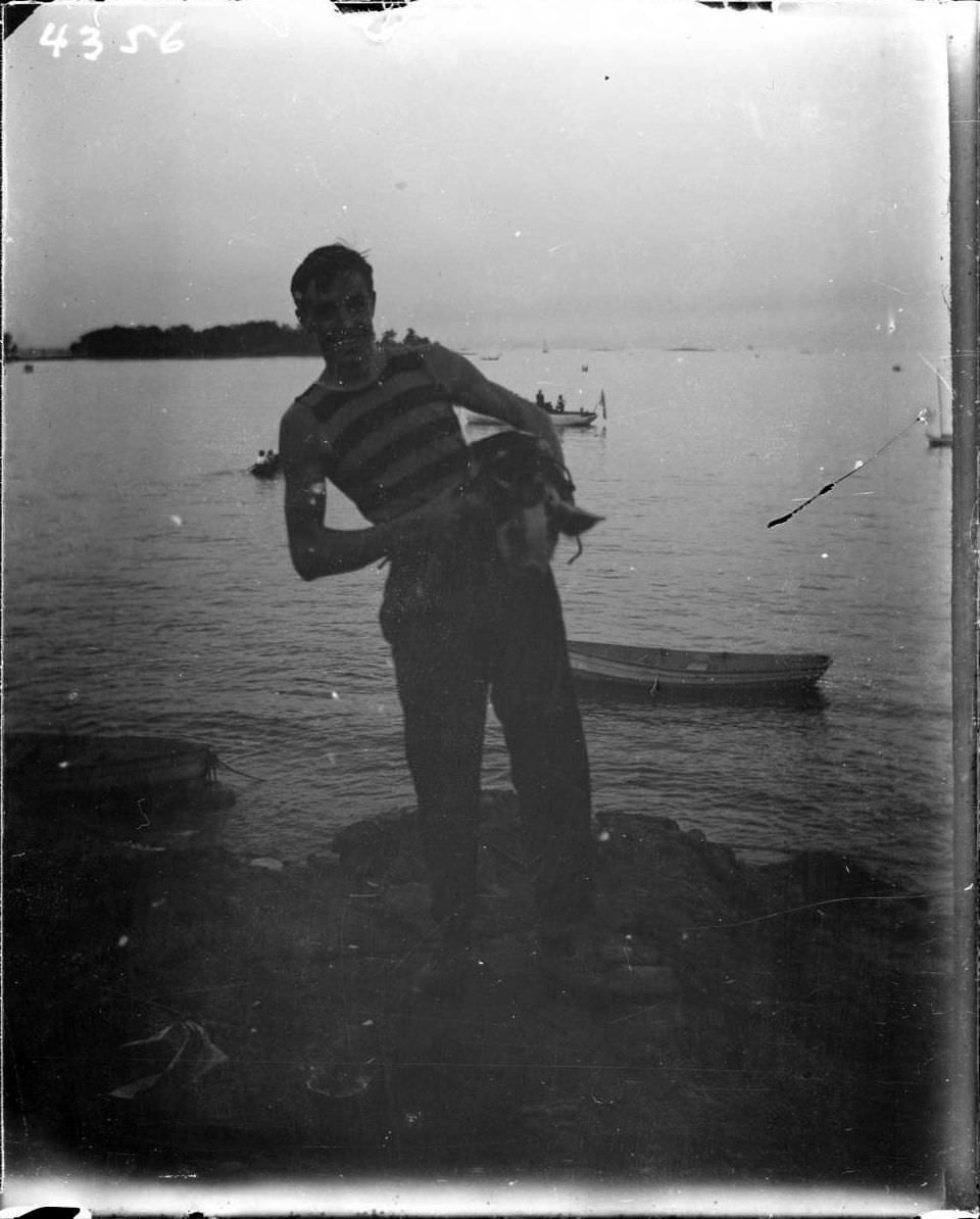 Young Man Standing On The Beach Holding A Pig At Orchard Beach, Bronx, 1907.