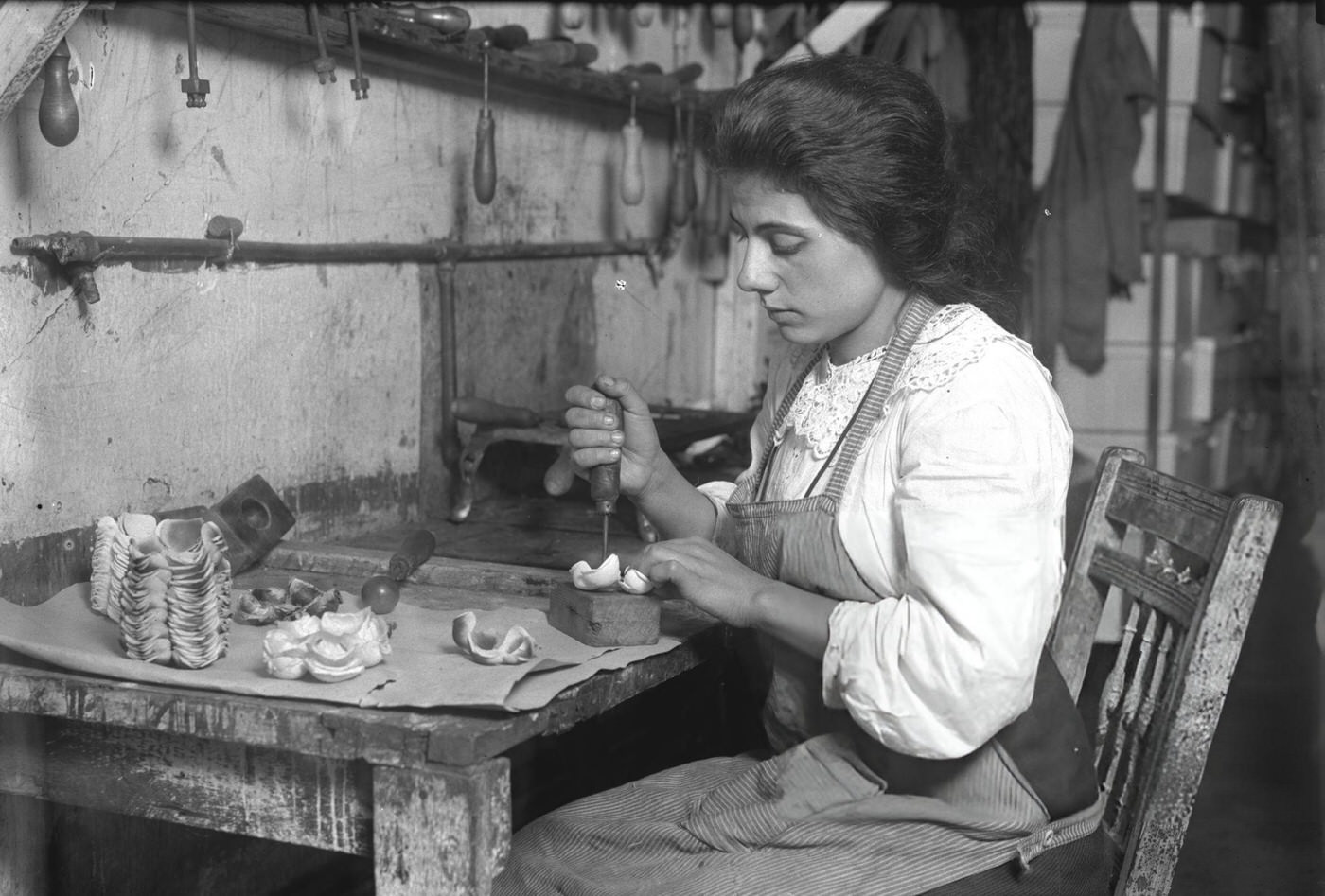 A Woman Punches A Hole In The Material While Making Artificial Roses In A Tenement Factory, Possibly In The Lower East Side, 1911.