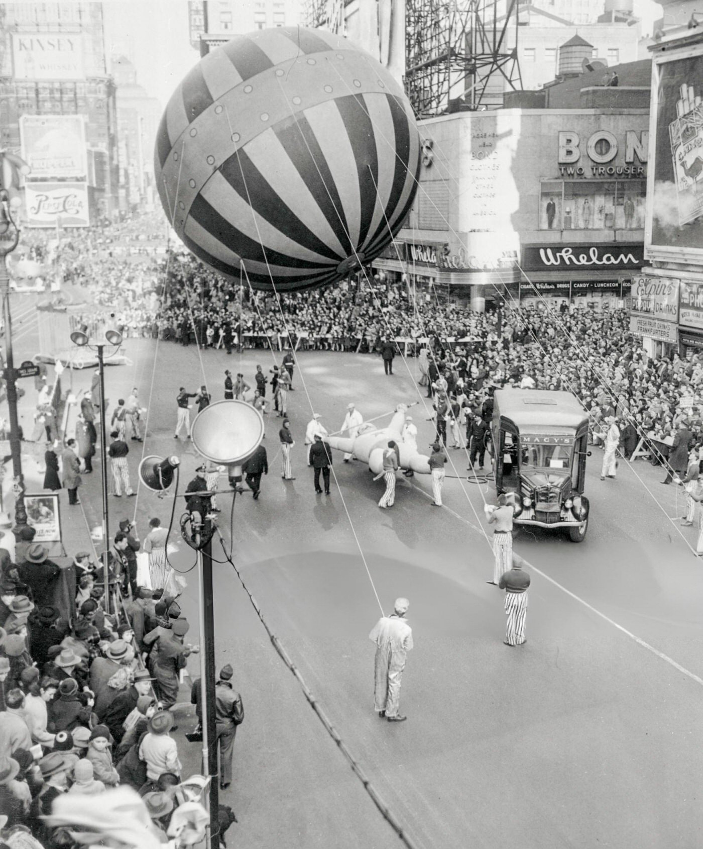 A Macy'S Truck With A Hose Attached To A Smaller Balloon With A Large, Round Balloon Being Flown Overhead During The Macy'S Thanksgiving Day Parade, 1939.