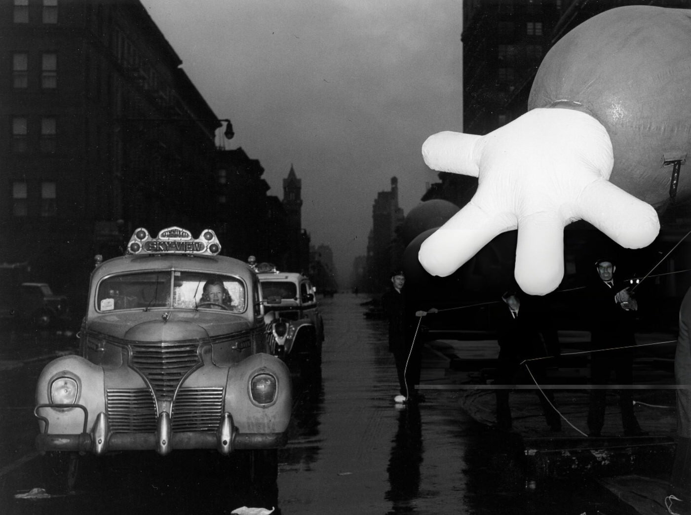 A Female Driver For Sky-View Taxis Passes The Giant Hand Of The Macy'S Clown Whilst Cruising Down Columbus Avenue, New York, Circa 1942.