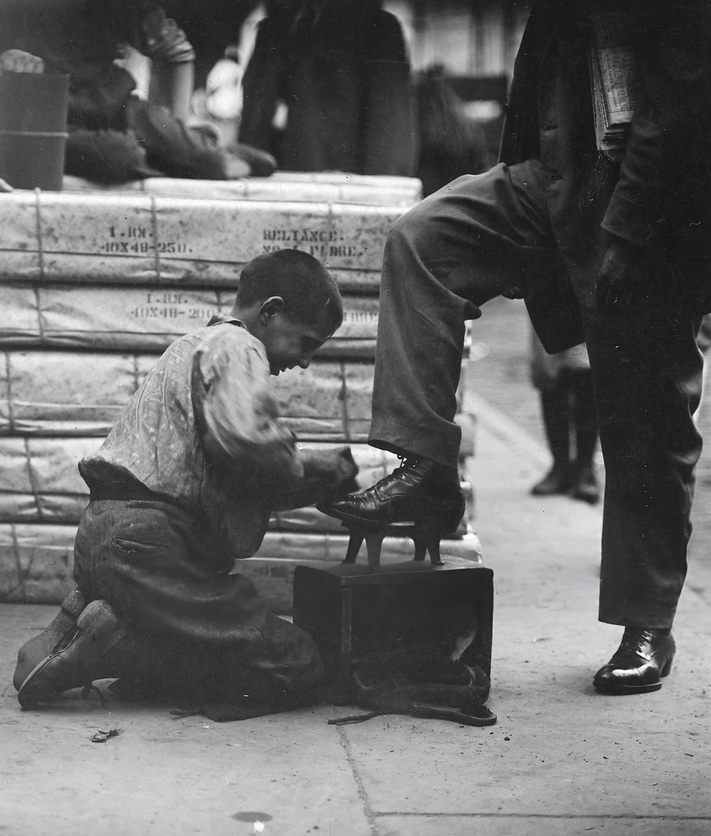 A Young Boy Shines Shoes On The Sidewalk Of The Bowery In Lower Manhattan, New York, June 1910.