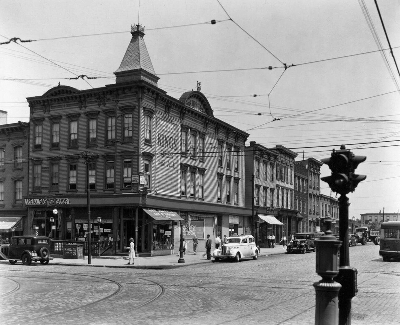 Clapboard Buildings, Cobblestone Streets With Trolley Tracks, Cars, And A Subway Entrance On The Corner At Graham And Metropolitan Avenues, Brooklyn, Circa 1937.