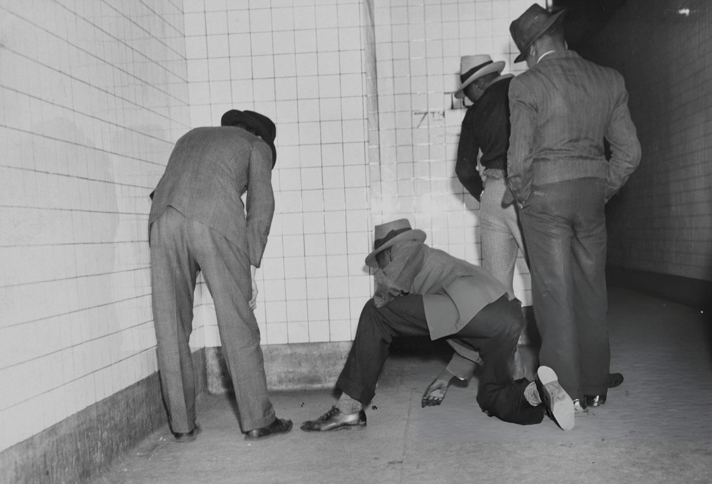 Rear View Of Men Playing A Dice Game Against A White-Tiled Subway Wall, Circa 1950.