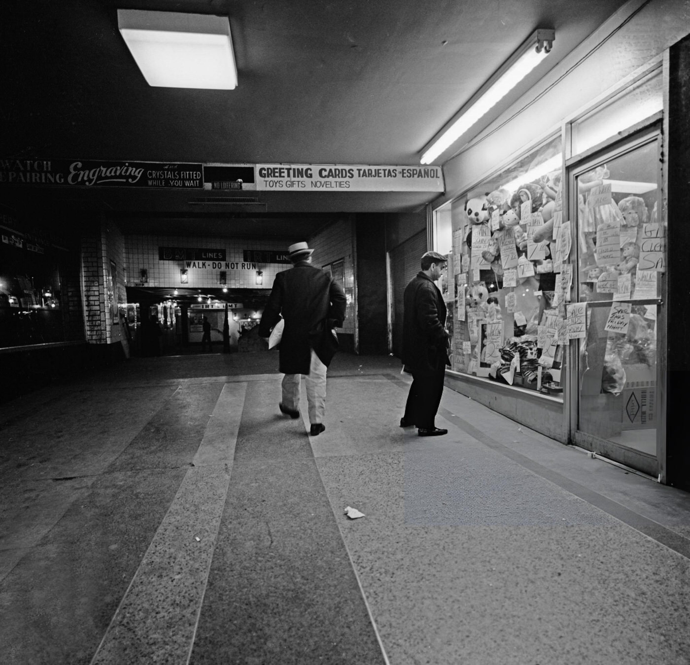 A Man Walks Up The Slope As A Second Man Stops To Look In The Window Of A Shop At The Times Square-42Nd Street/Port Authority Bus Terminal Subway Station, January 22, 1964.