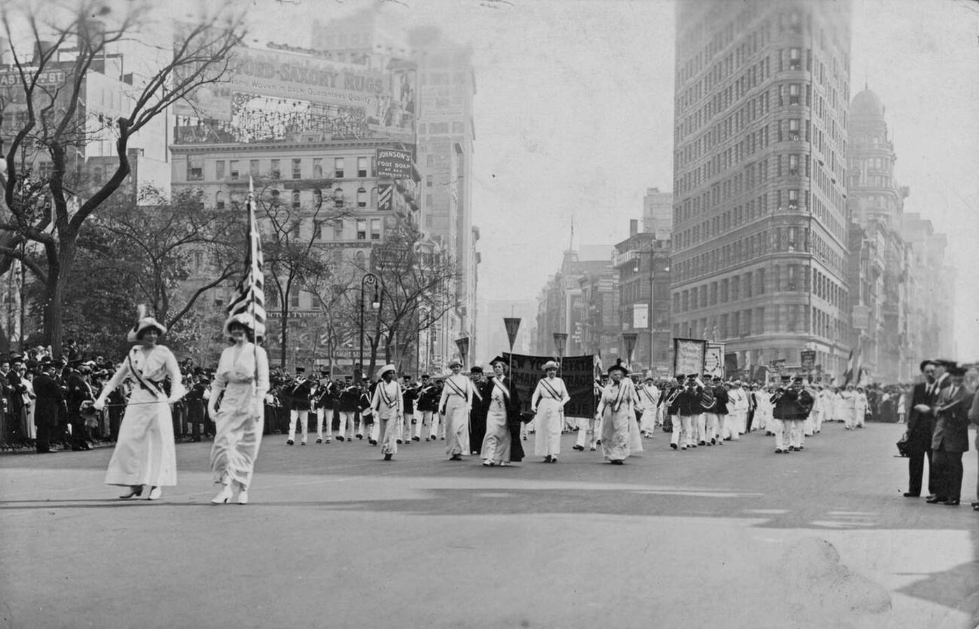 Women, Wearing White Edwardian Clothing And Sashes, Followed By A Marching Band, Taking Part In A Suffrage Parade In New York City, 1913.