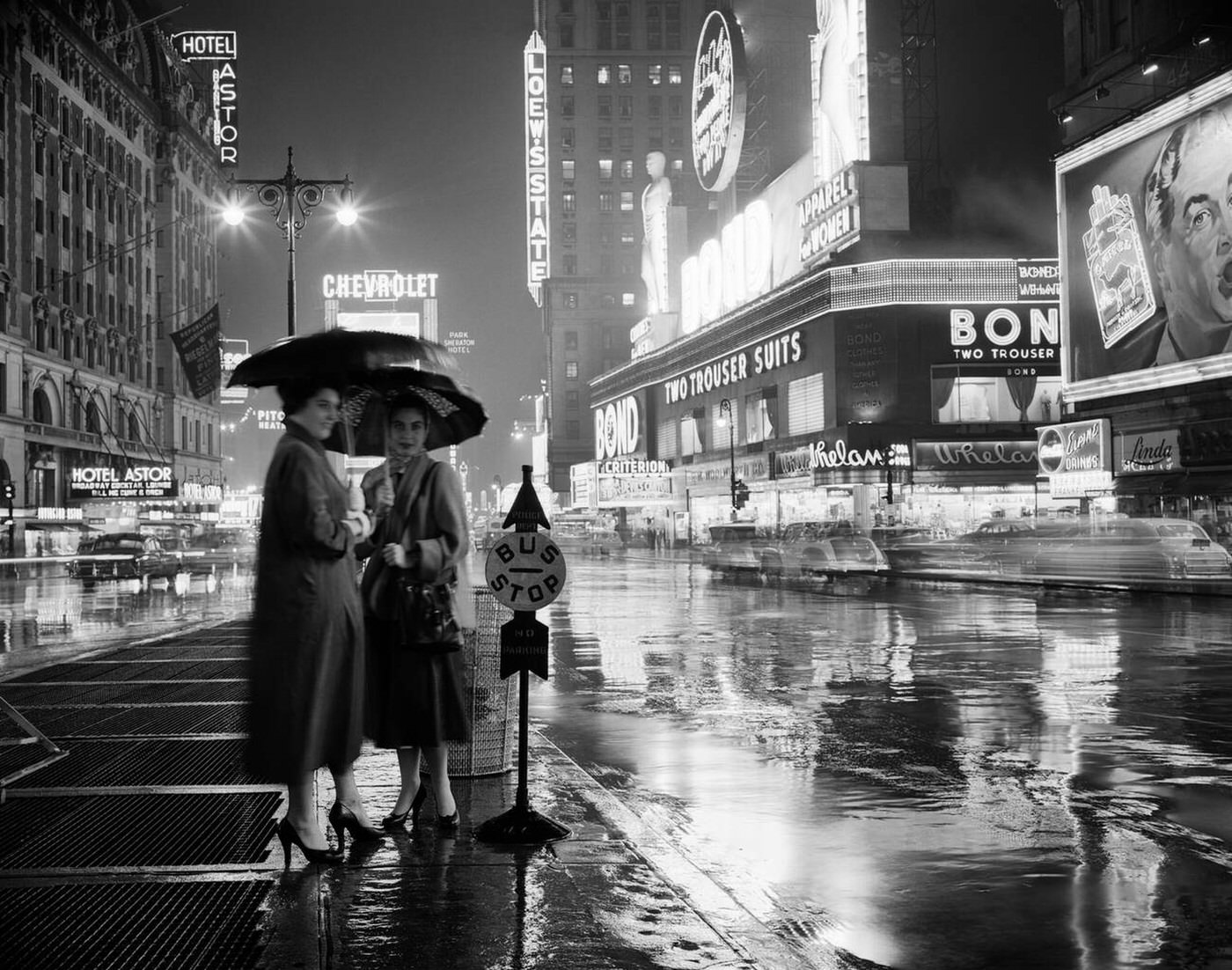 Two Silhouetted Women At A Bus Stop Under Umbrellas On A Rainy Night In Times Square, August 1, 1953.