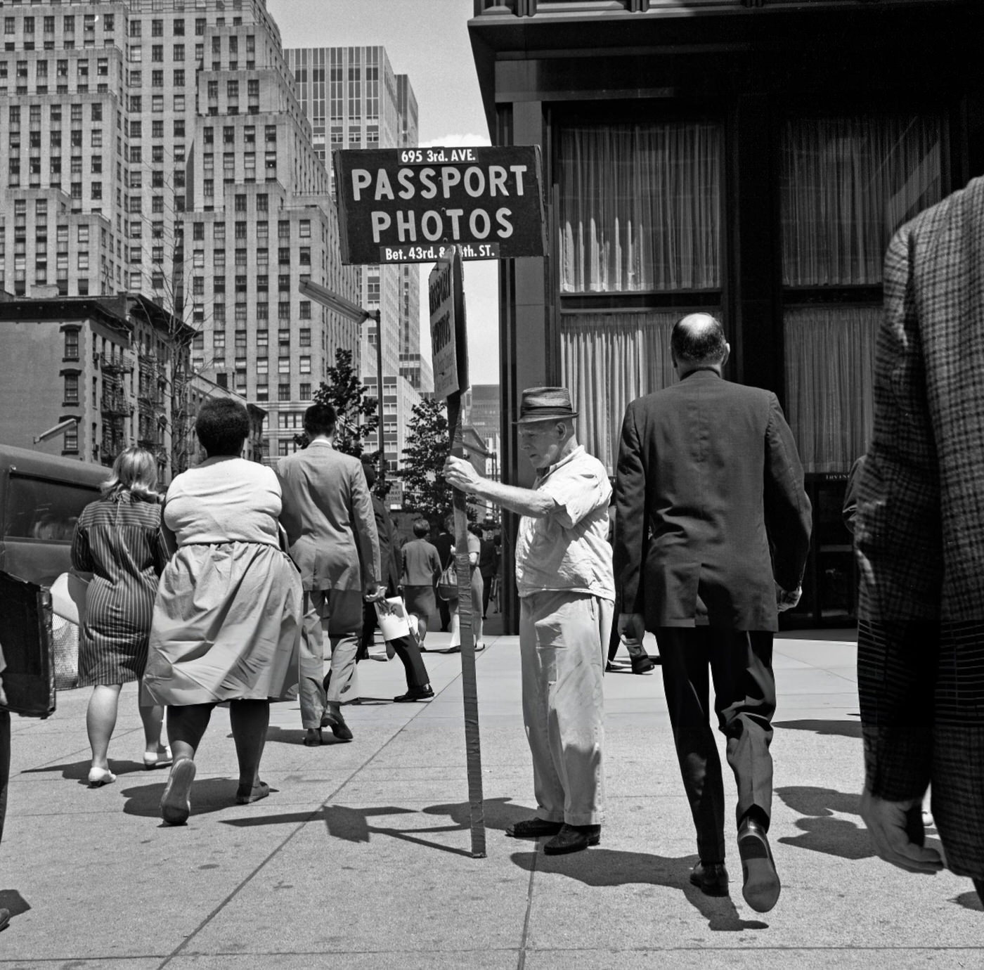 A Man Holding A Passport Photos Sign Advertising A Local Small Business, Stands On A Street Corner Near Times Square, June 1, 1967.