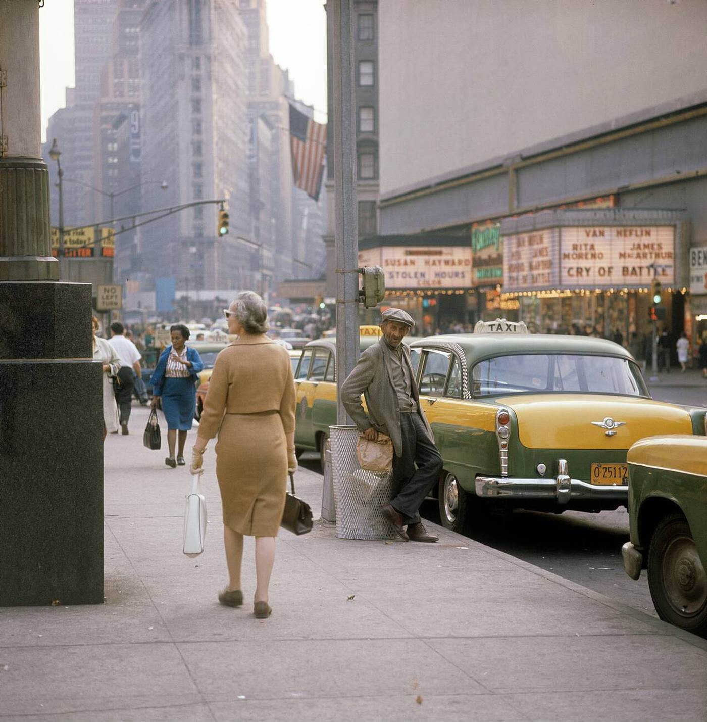 Street Scene With Cars, Buses And Taxis Driving On Broadway In Times Square, Showing Movie Theatres And A Woman With A Paper Bag, 1964.