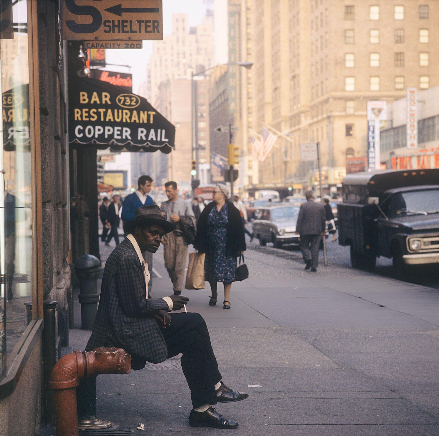 A Street Scene With A Man Sitting In Front Smoking, 1964.