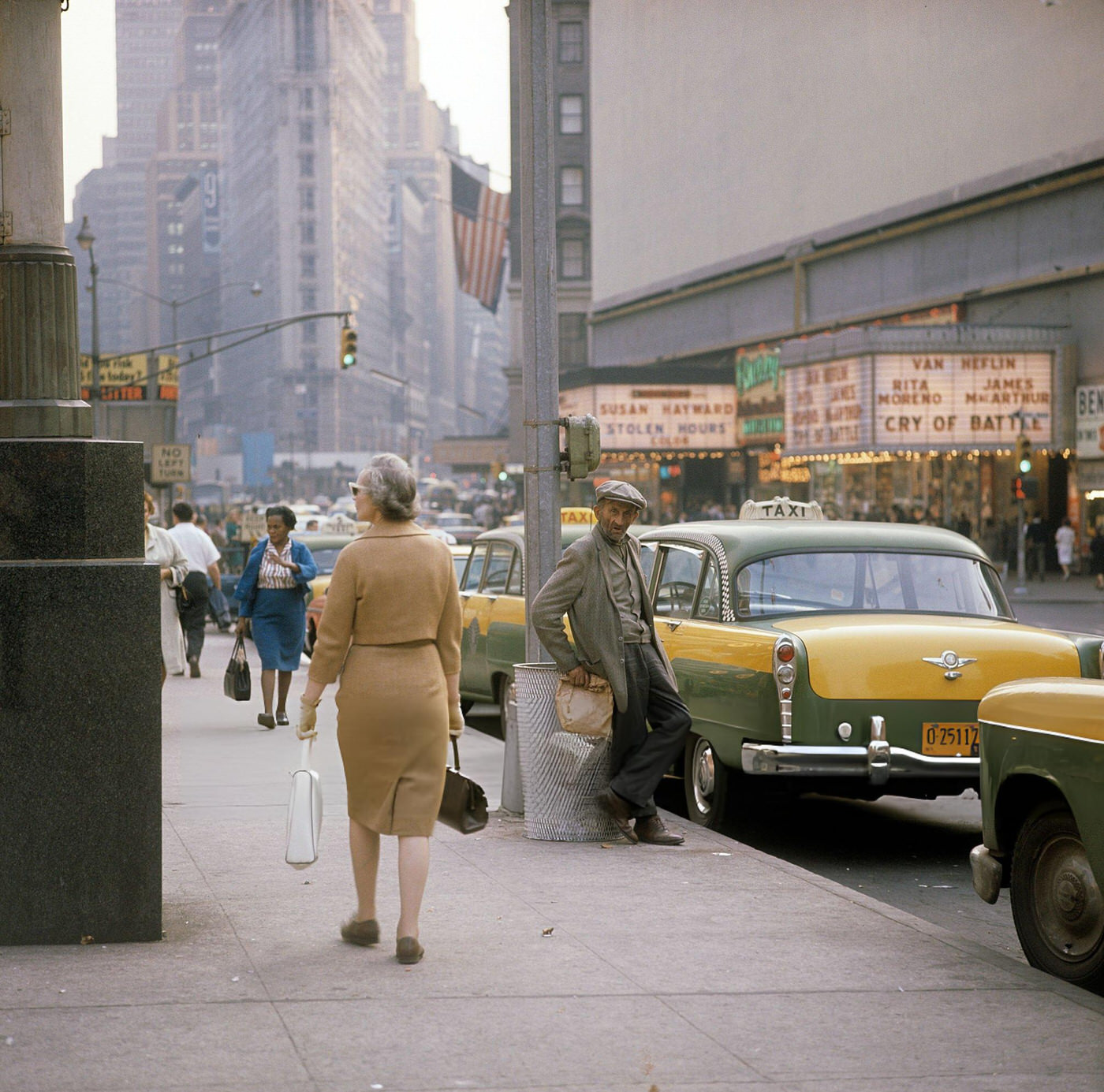 A Street Scene With Cars, Buses And Taxis Driving On Broadway In Times Square, Showing Movie Theatres And A Woman With A Paper Bag, 1964.