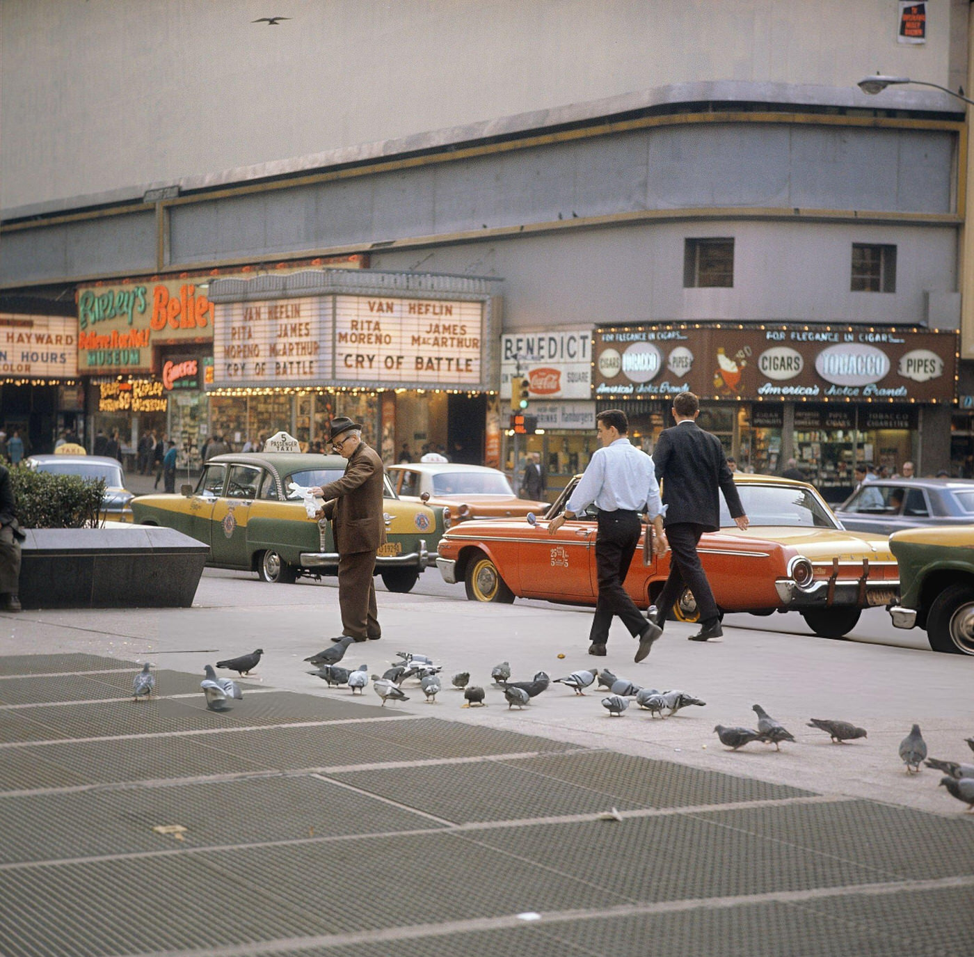 A Street Scene With Cars And Taxis Driving On Broadway In Times Square, Showing Movie Theatres And An Elderly Man Feeding Pigeons, 1964.