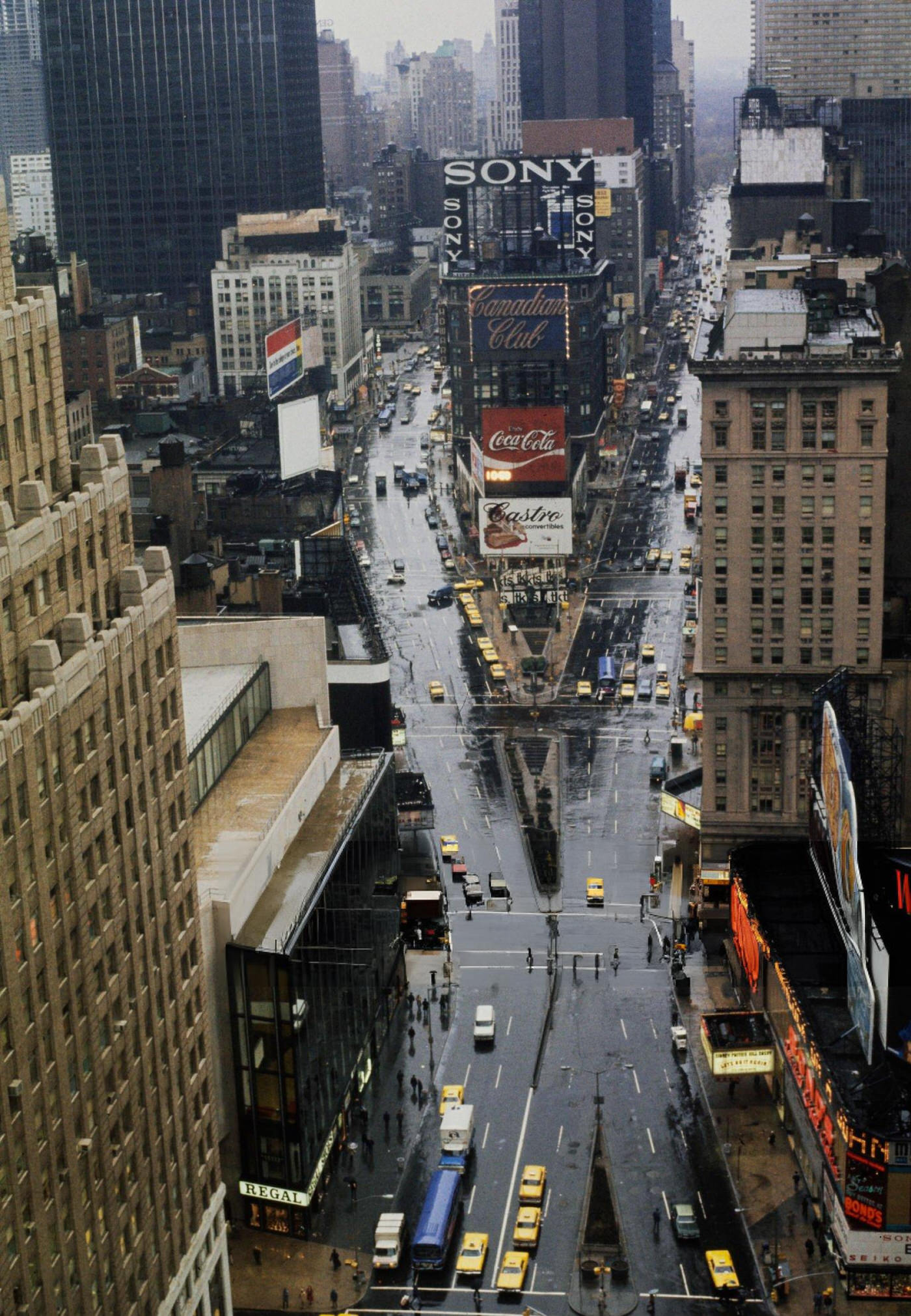 A Street Scene With Cars, Buses And Taxis Driving On Broadway In Times Square, Showing Movie Theatres And A Woman With A Paper Bag, 1964.