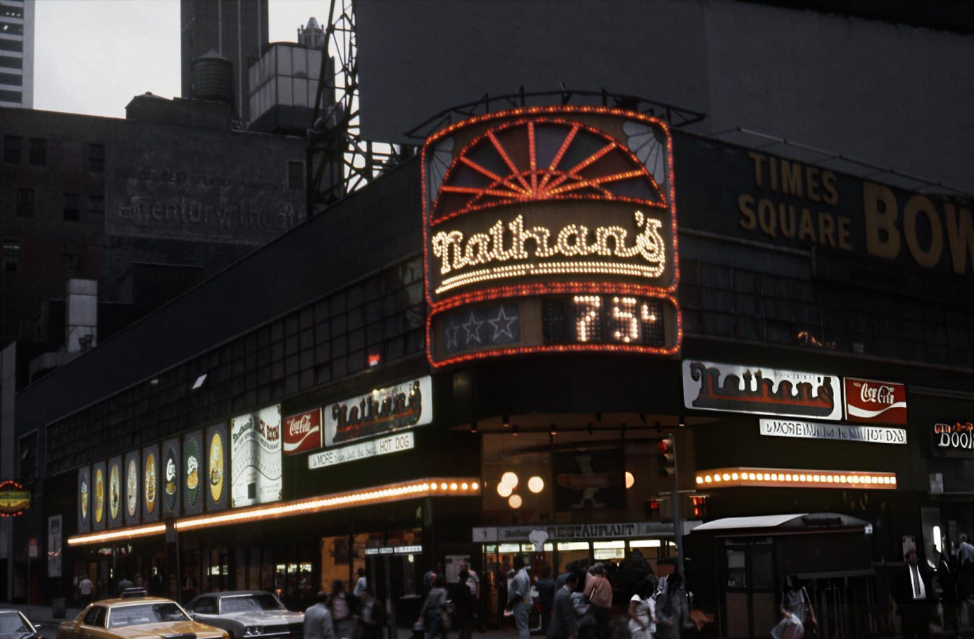 A Street Scene With Cars And Taxis Driving On Broadway In Times Square, Showing Movie Theatres And An Elderly Man Feeding Pigeons, 1964.