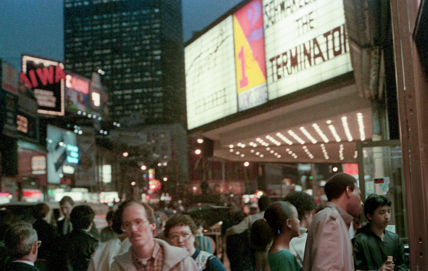 People In Times Square Pass A Cinema Marquee Featuring 'The Terminator', November 1, 1984.