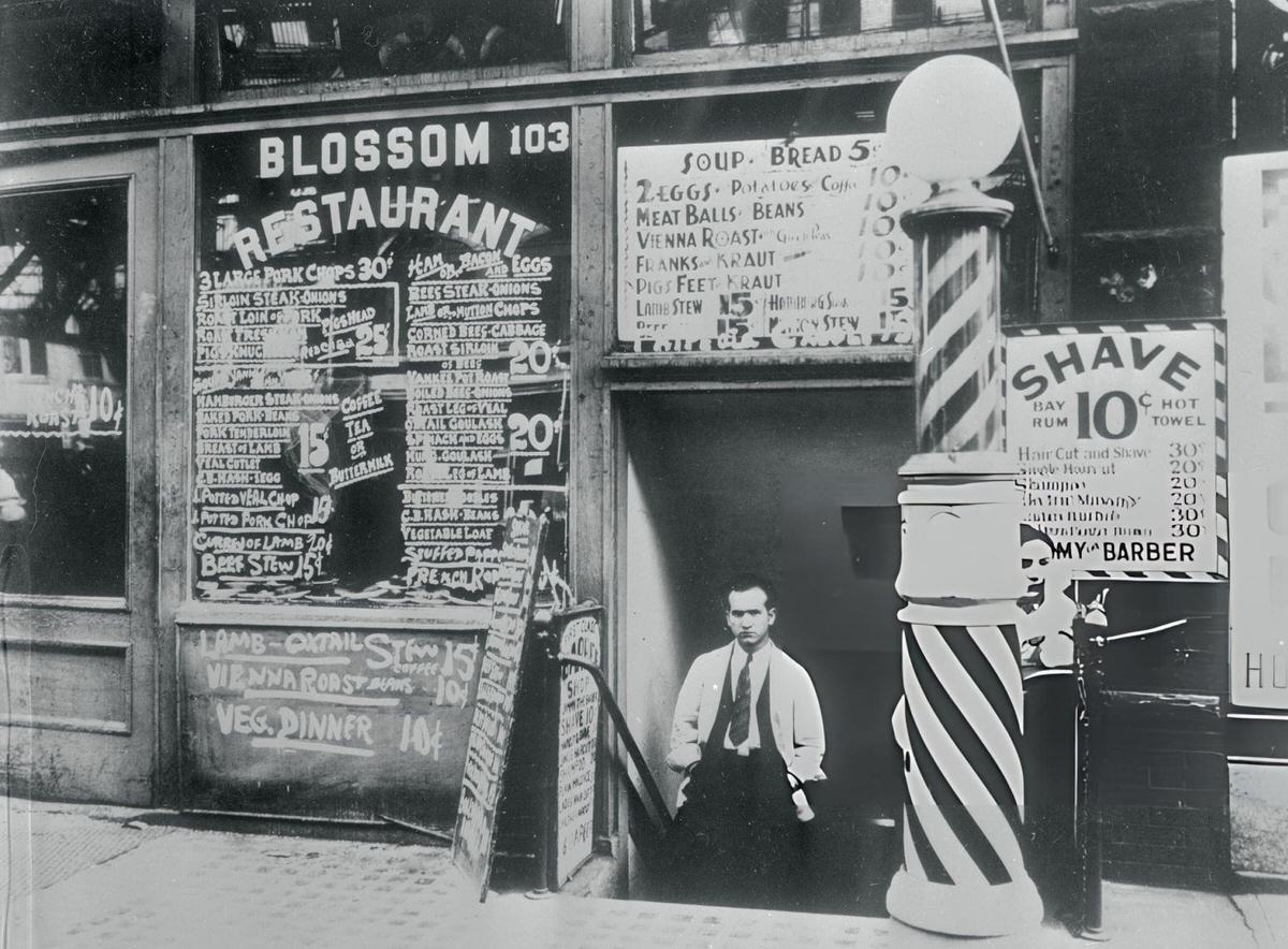 Barber Sitting In Front Of A Shop With A Barber Pole In Downtown New York.