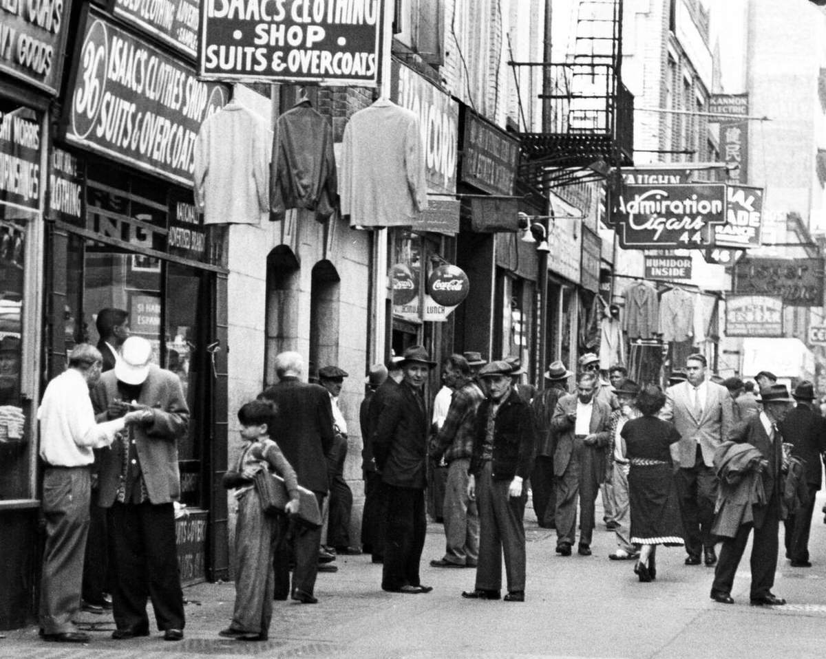Pedestrians In Tailored Suits And Hats Walking Past Clothing And Cigar Shops On The Bowery, New York, 1940S.