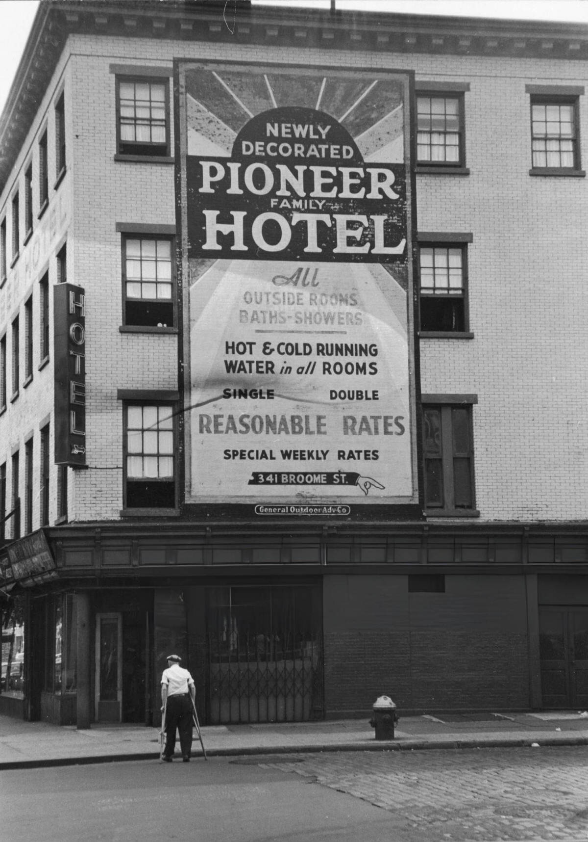 Man On Crutches Crossing Broome Street At The Bowery In Front Of The Pioneer Hotel, New York, 1964.