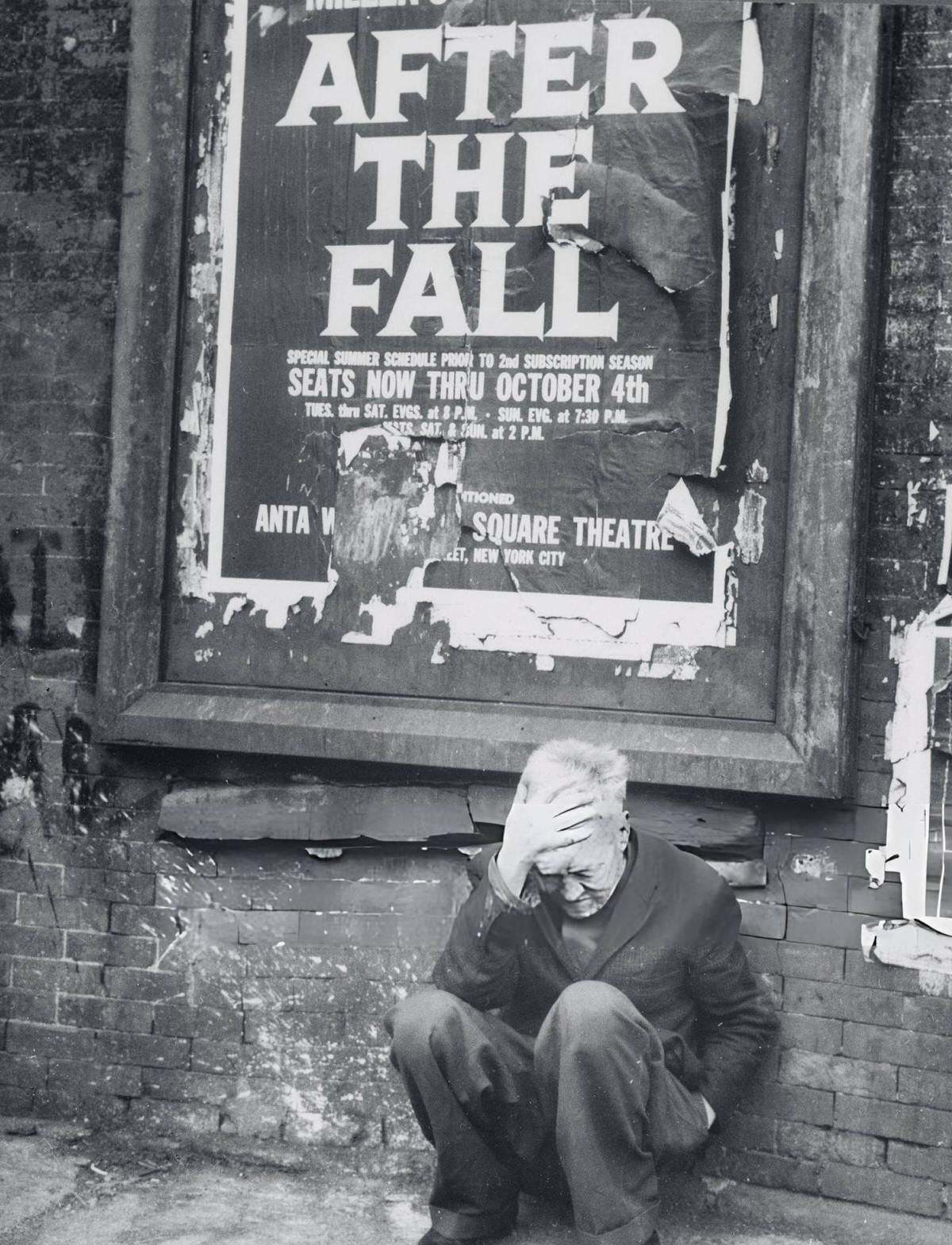 Man Crouching Beneath A Tattered Poster In The Bowery, New York.