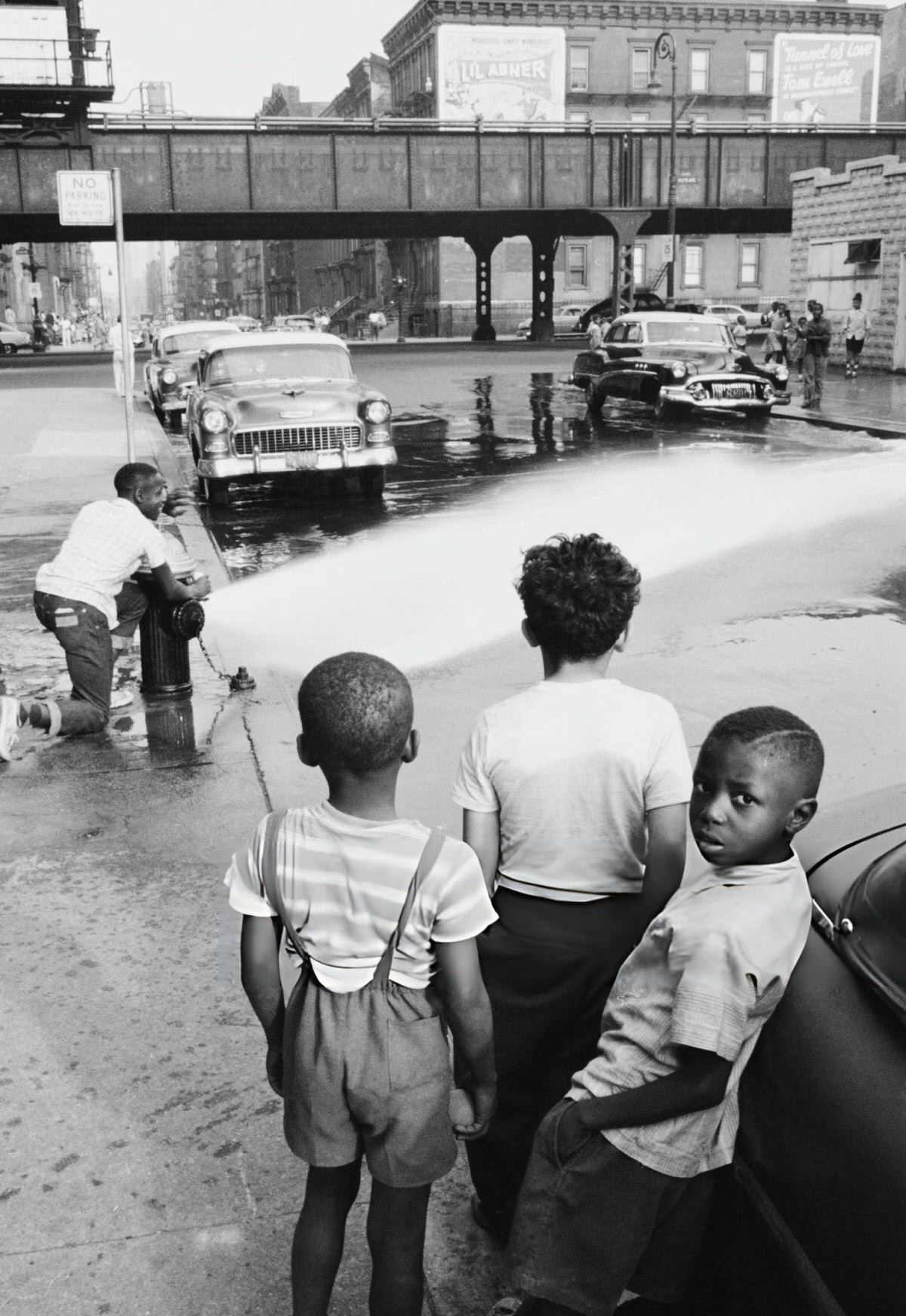 Children Playing In The Street While A Man Adjusts A Fire Hydrant, Harlem, 1957.