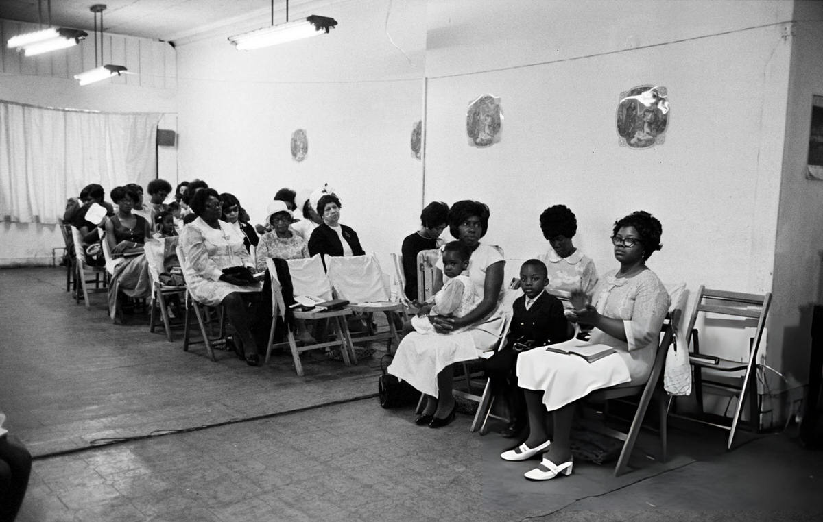 Women And Children Sitting On Folding Chairs In A Place Of Prayer, Harlem, 1970.