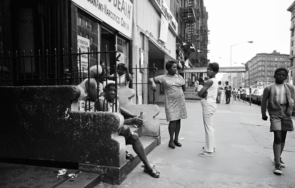 Women Gathered Outside A Building Entrance While A Boy Walks Toward The Camera, Harlem, 1970.