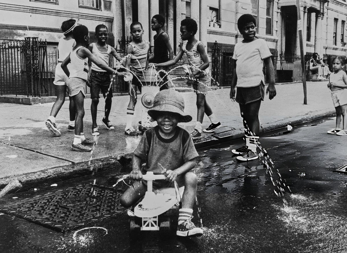 Children Playing In Water From A Fire Hydrant, Harlem, 1975.